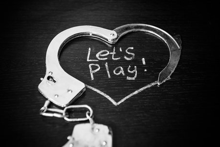 Lets play bdsm. Handcuffs for role-playing games like heart. Handcuffs with caption on black background.
