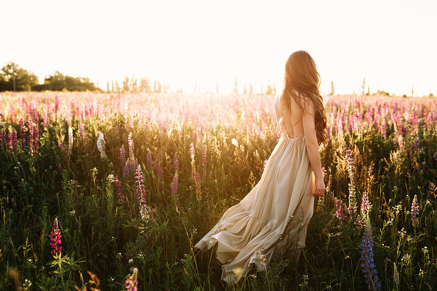 Young woman walking on flower field at sunset on background. Horizontal view with copy space.